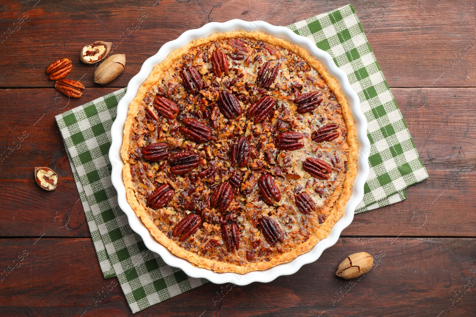 Photo of Delicious pecan pie in baking dish and fresh nuts on wooden table, top view