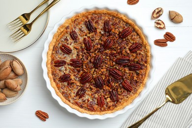 Photo of Delicious pecan pie in baking dish, fresh nuts and cake server on white wooden table, flat lay