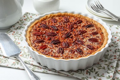 Photo of Delicious pecan pie in baking dish and cake server on white table