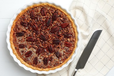 Photo of Delicious pecan pie in baking dish and knife on white wooden table, flat lay