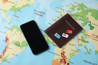 Photo of SIM cards, smartphone and passport on world map, flat lay