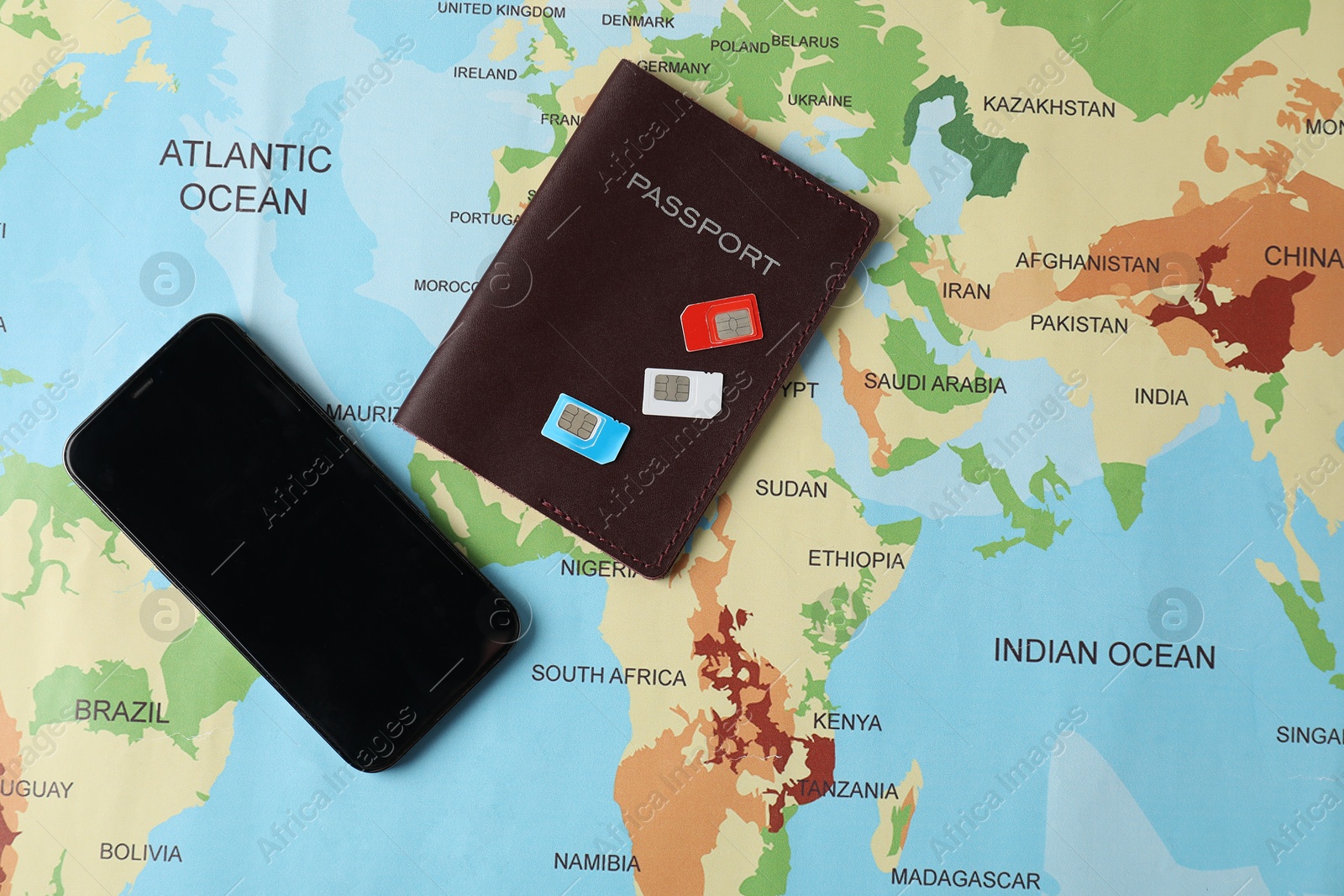 Photo of SIM cards, smartphone and passport on world map, flat lay