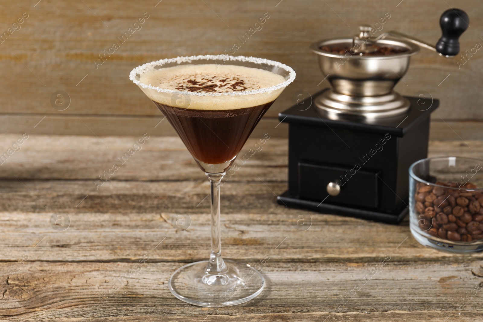 Photo of Glass of fresh cocktail, manual coffee grinder and beans in bowl on wooden table