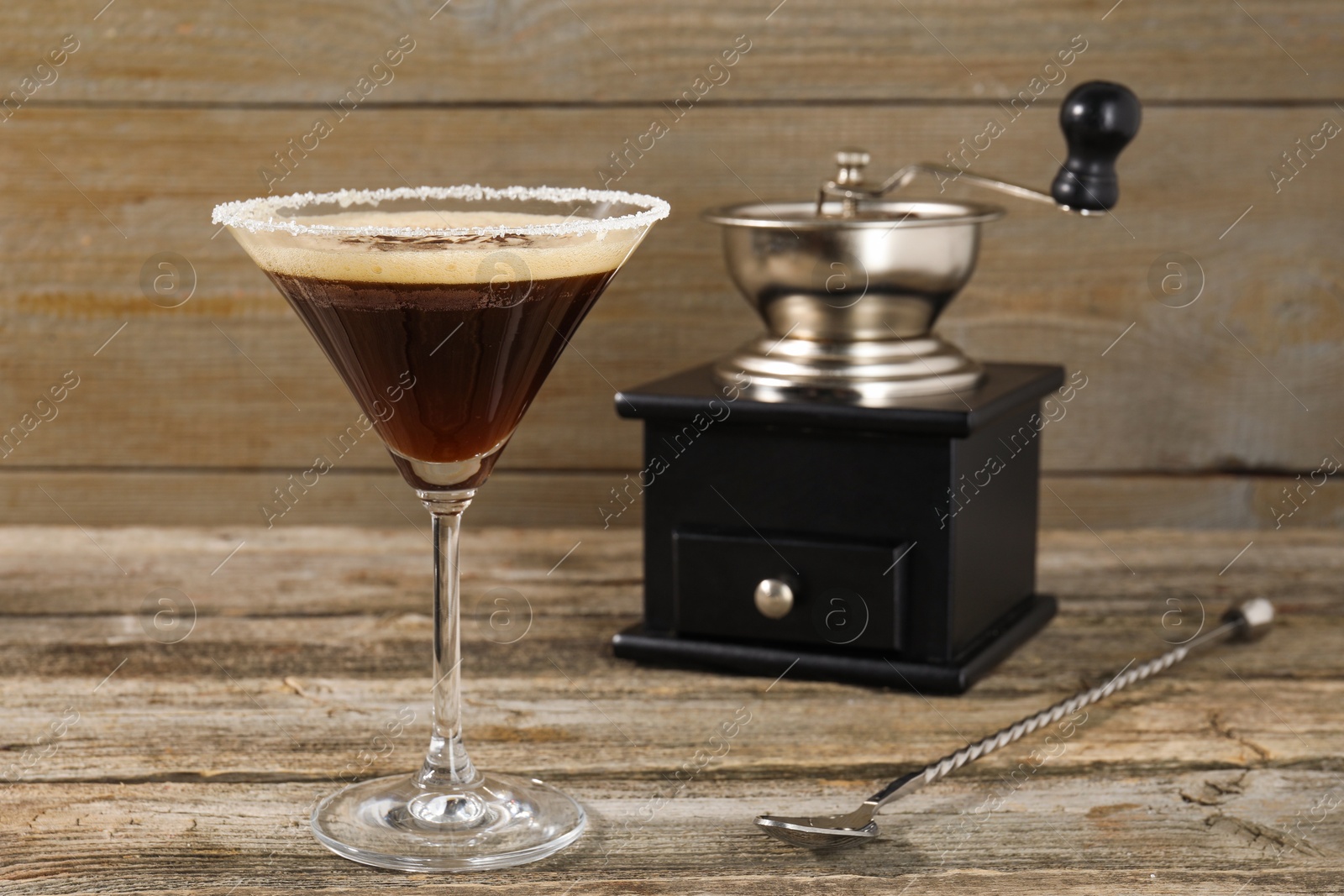 Photo of Glass of fresh cocktail, manual coffee grinder and mixing spoon on wooden table