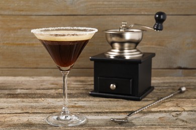 Photo of Glass of fresh cocktail, manual coffee grinder and mixing spoon on wooden table