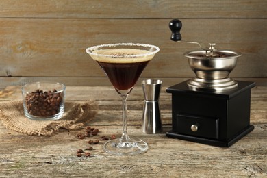 Photo of Glass of fresh cocktail, manual coffee grinder, beans in bowl and jigger on wooden table