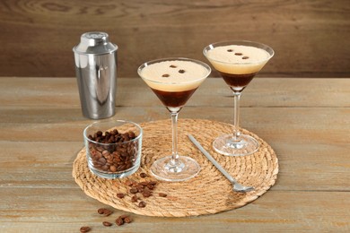 Photo of Glasses of fresh coffee cocktail, shaker, beans in bowl and mixing spoon on wooden table