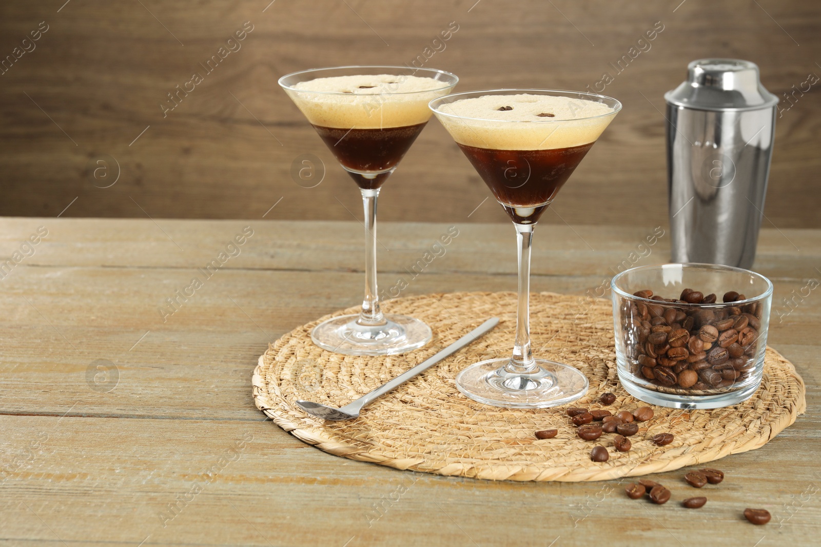 Photo of Glasses of fresh coffee cocktail, shaker, beans in bowl and mixing spoon on wooden table, space for text