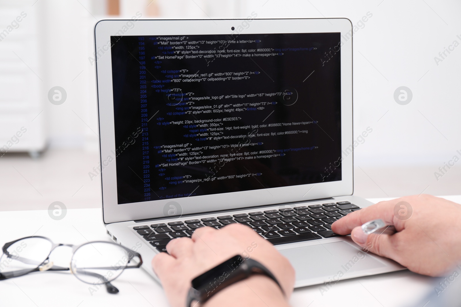 Photo of Programmer working with laptop at white desk in office, closeup