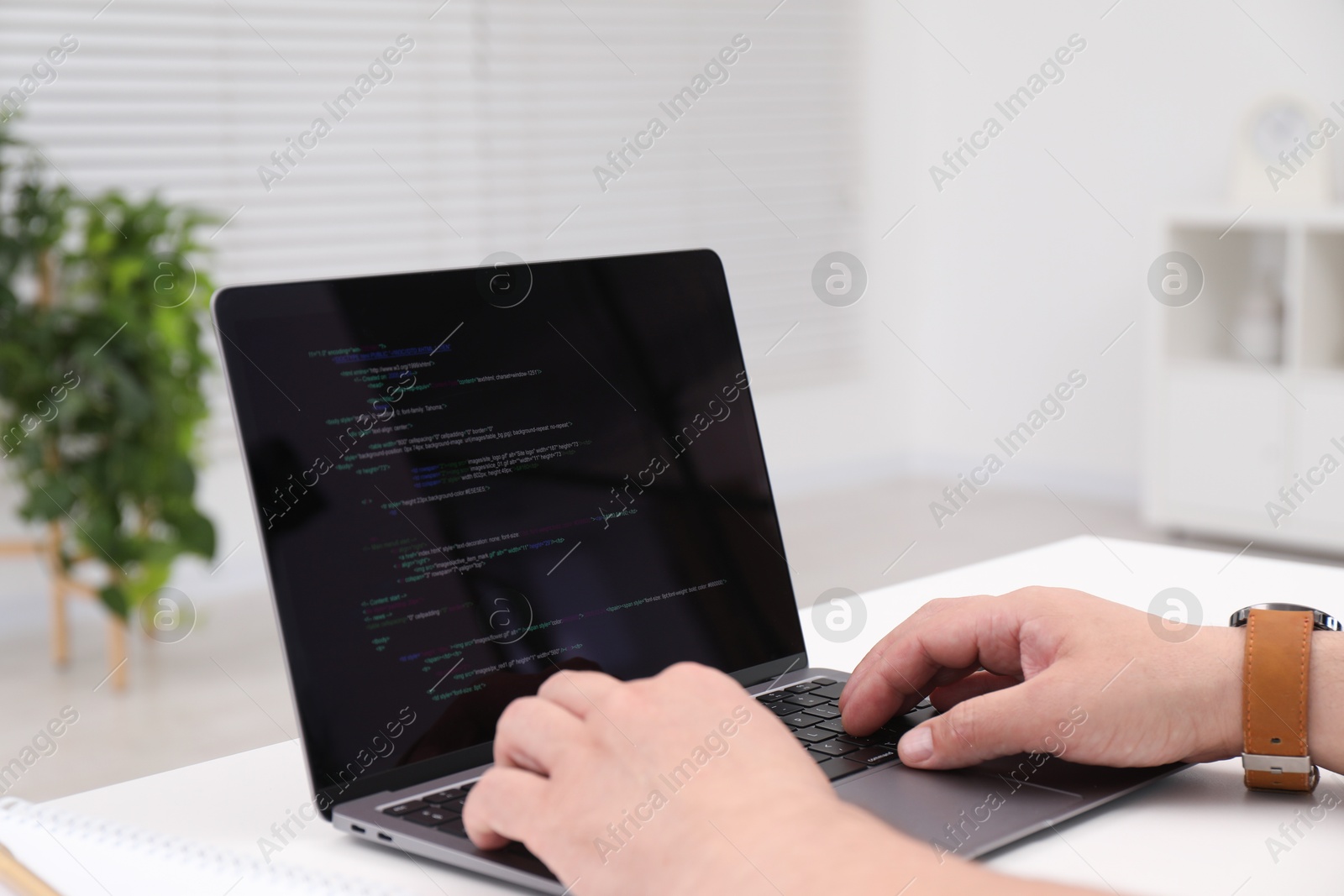 Photo of Programmer working with laptop at white desk in office, closeup