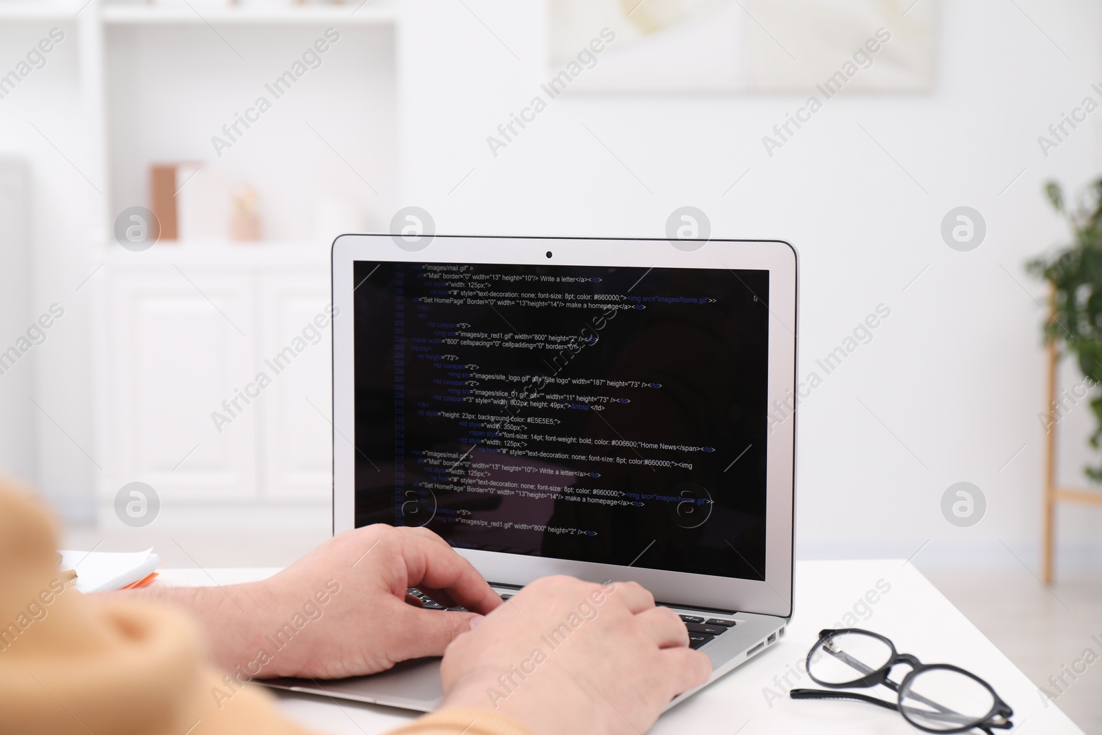 Photo of Programmer working with laptop at white desk in office, closeup