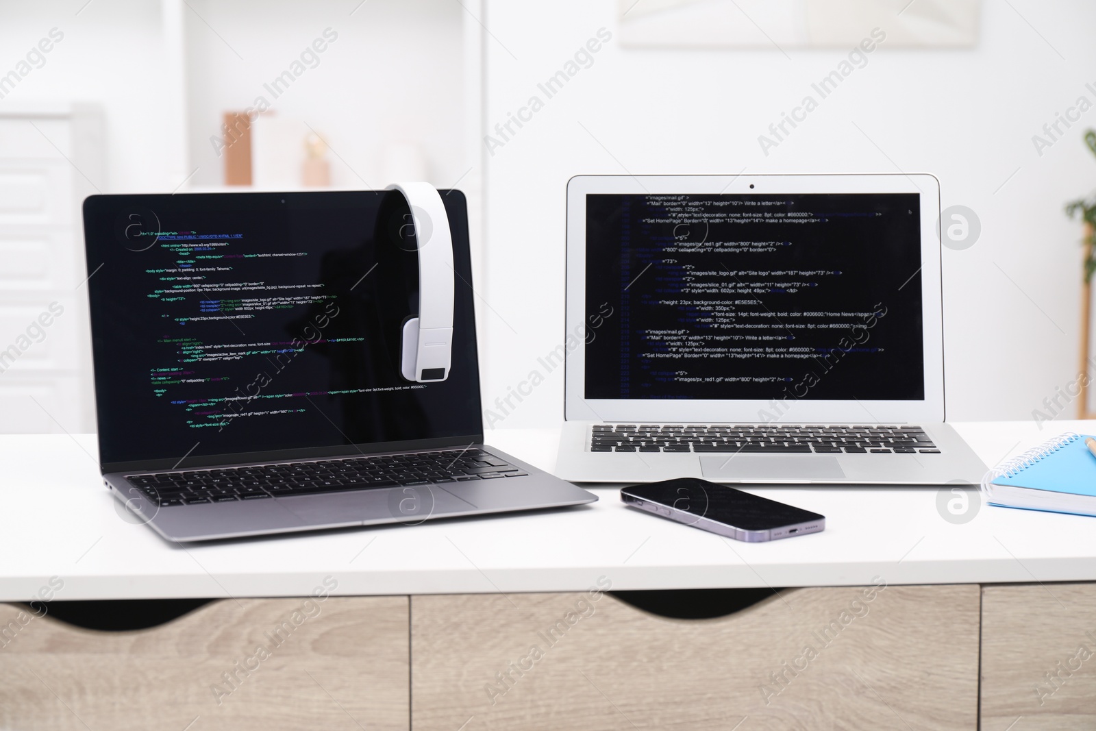 Photo of Programmer's workplace. Modern laptops with unfinished code, headphones and smartphone on desk indoors