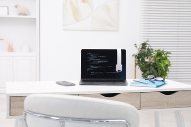 Photo of Programmer's workplace. Modern laptop with unfinished code, headphones and other supplies on desk indoors