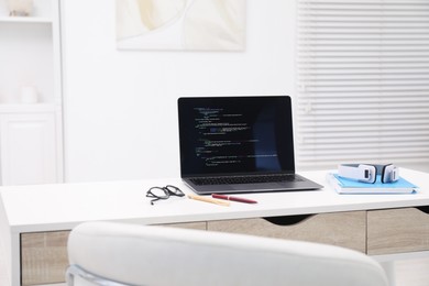 Photo of Programmer's workplace. Modern laptop with unfinished code, headphones and other supplies on desk indoors