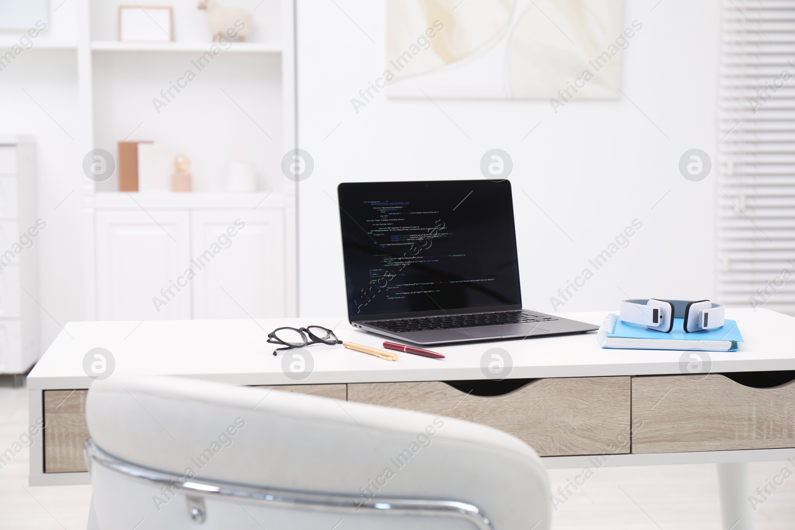 Photo of Programmer's workplace. Modern laptop with unfinished code, headphones and other supplies on desk indoors