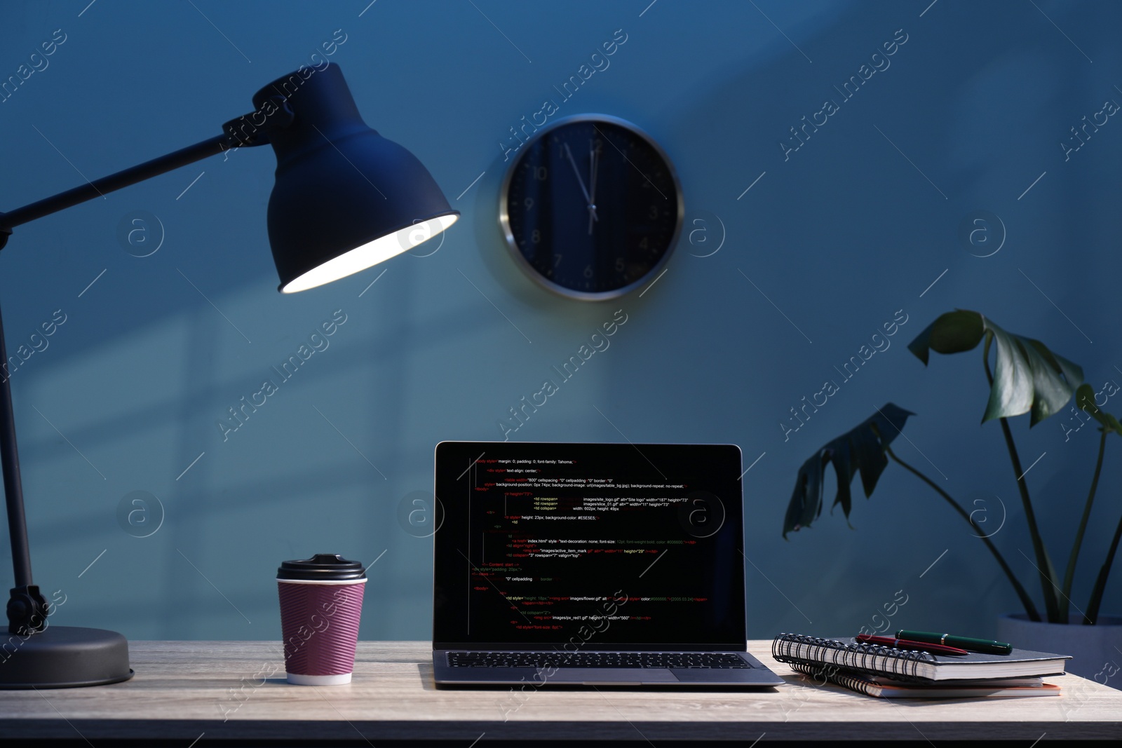 Photo of Programmer's workplace. Modern laptop with unfinished code, lamp and other supplies on wooden desk indoors