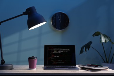 Photo of Programmer's workplace. Modern laptop with unfinished code, lamp and other supplies on wooden desk indoors