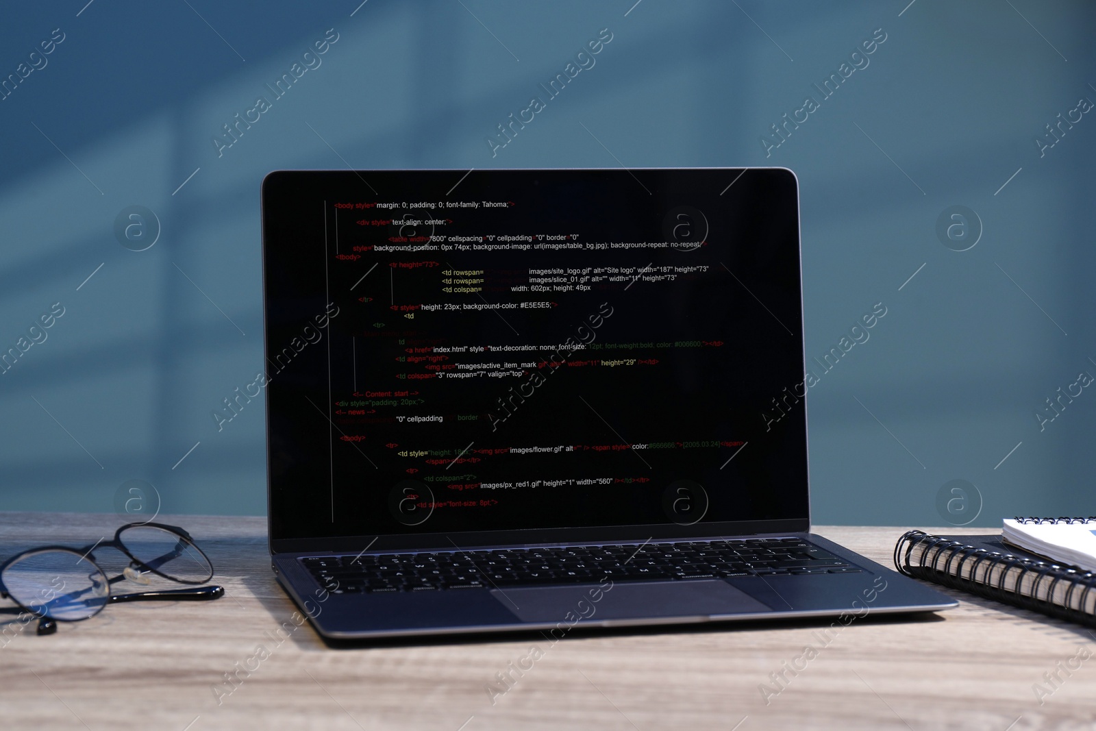 Photo of Programmer's workplace. Modern laptop with unfinished code, glasses and notebooks on wooden desk