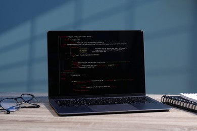 Programmer's workplace. Modern laptop with unfinished code, glasses and notebooks on wooden desk