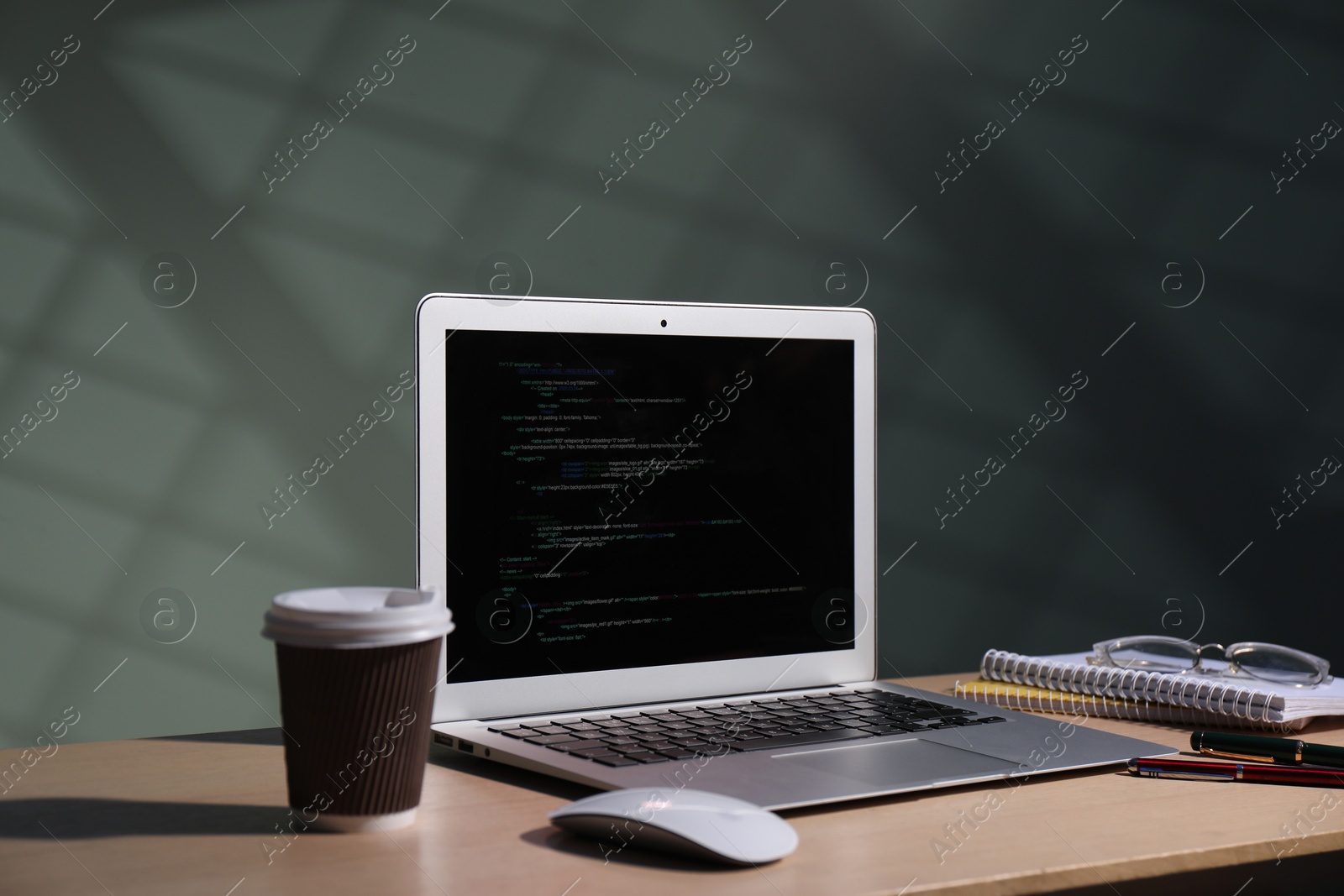 Photo of Programmer's workplace. Modern laptop with unfinished code and other supplies on wooden desk