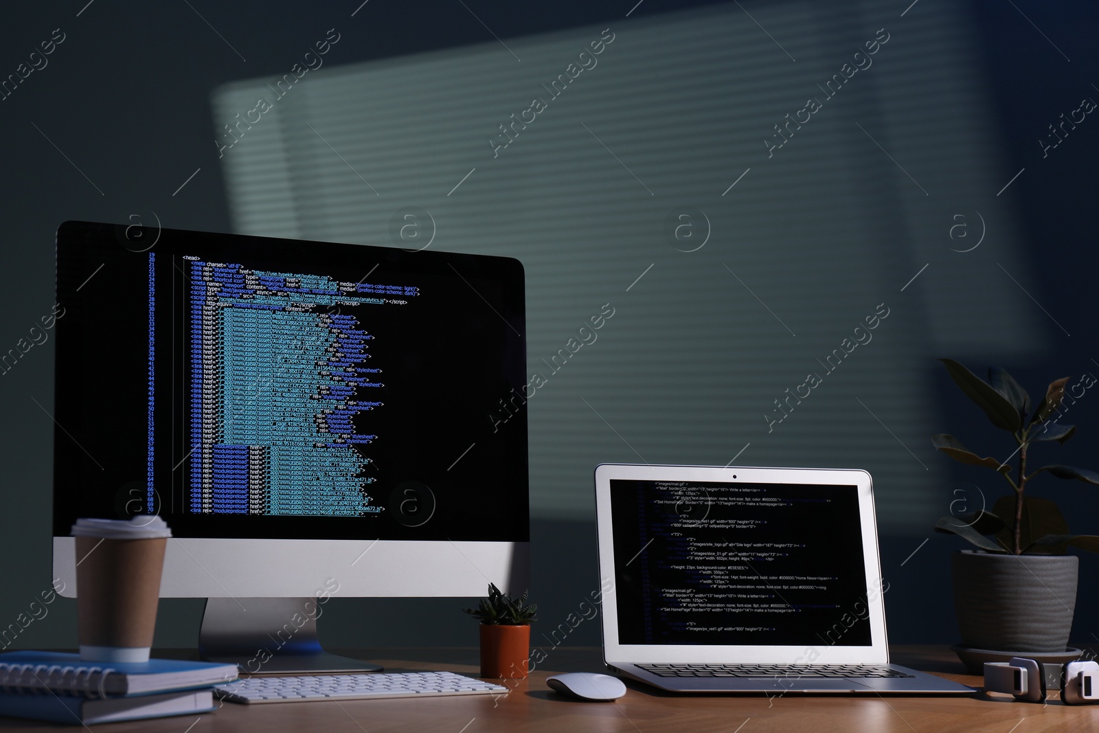 Photo of Programmer's workplace. Modern computer with unfinished code, laptop and other supplies on wooden desk