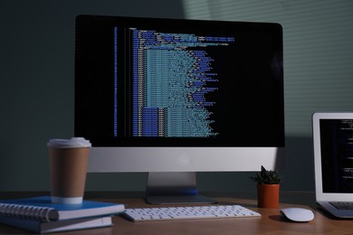 Photo of Programmer's workplace. Modern computer with unfinished code, laptop and other supplies on wooden desk