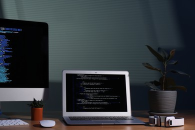 Photo of Programmer's workplace. Modern computer with unfinished code, laptop and other supplies on wooden desk