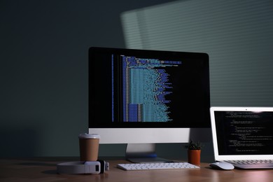 Photo of Programmer's workplace. Modern computer with unfinished code, laptop and other supplies on wooden desk