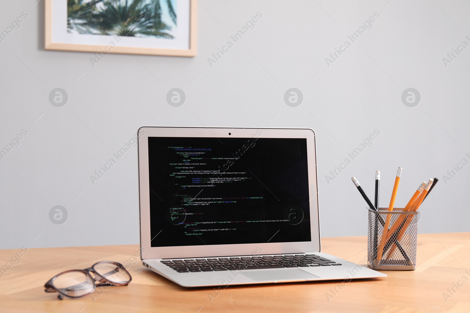 Photo of Programmer's workplace. Modern laptop with unfinished code, glasses and stationery on desk indoors