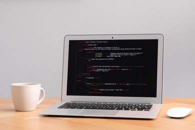 Photo of Programmer's workplace. Modern laptop with unfinished code and cup on desk indoors