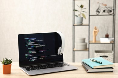 Photo of Programmer's workplace. Modern laptop with unfinished code, stationery and houseplant on desk indoors