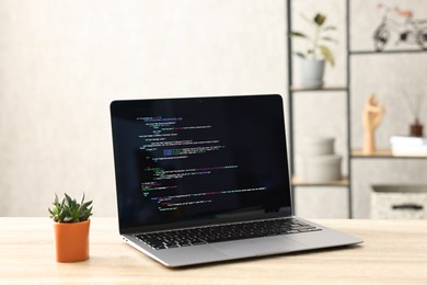 Photo of Programmer's workplace. Modern laptop with unfinished code and houseplant on desk indoors