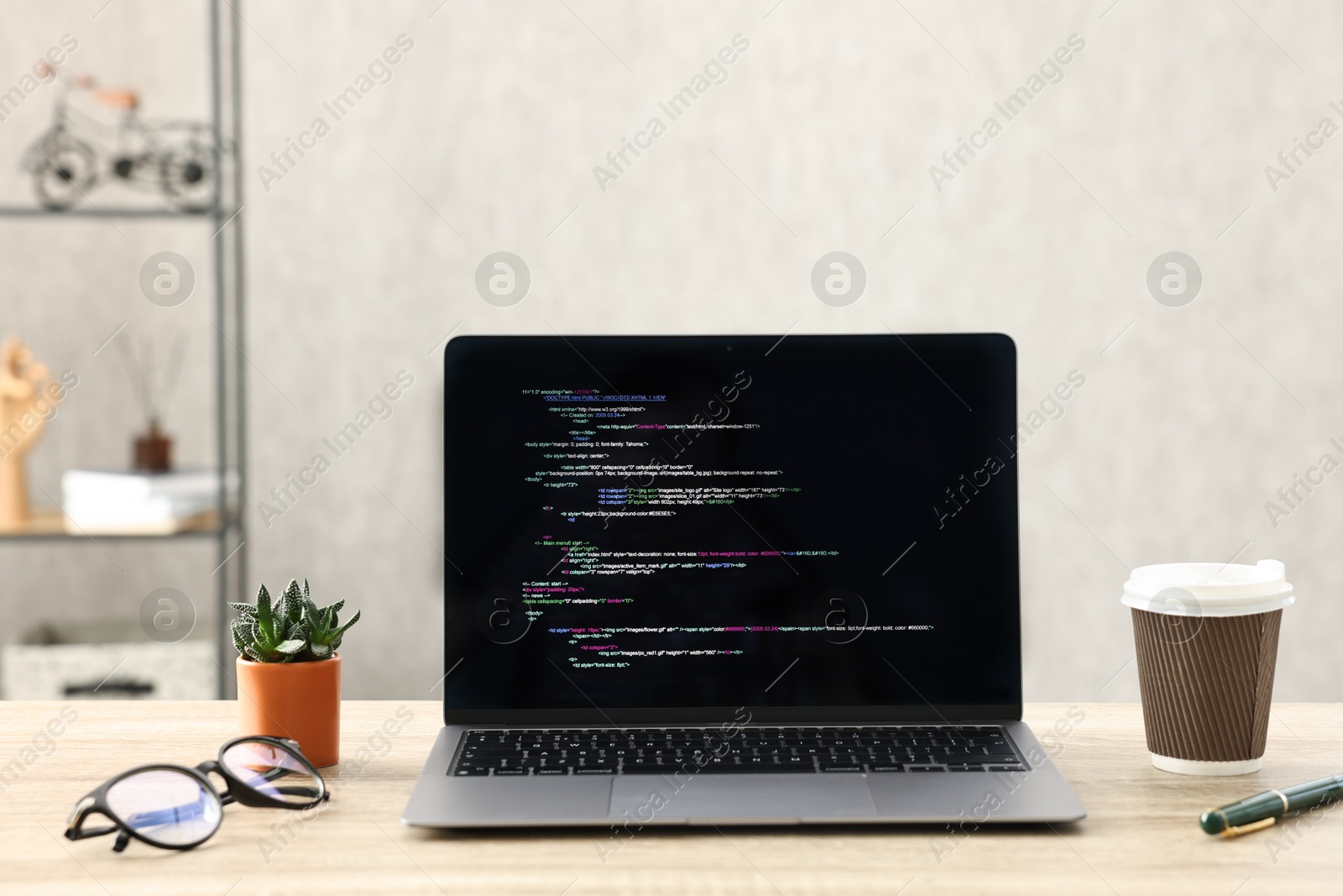 Photo of Programmer's workplace. Modern laptop with unfinished code, paper cup of drink, glasses and houseplant on desk indoors