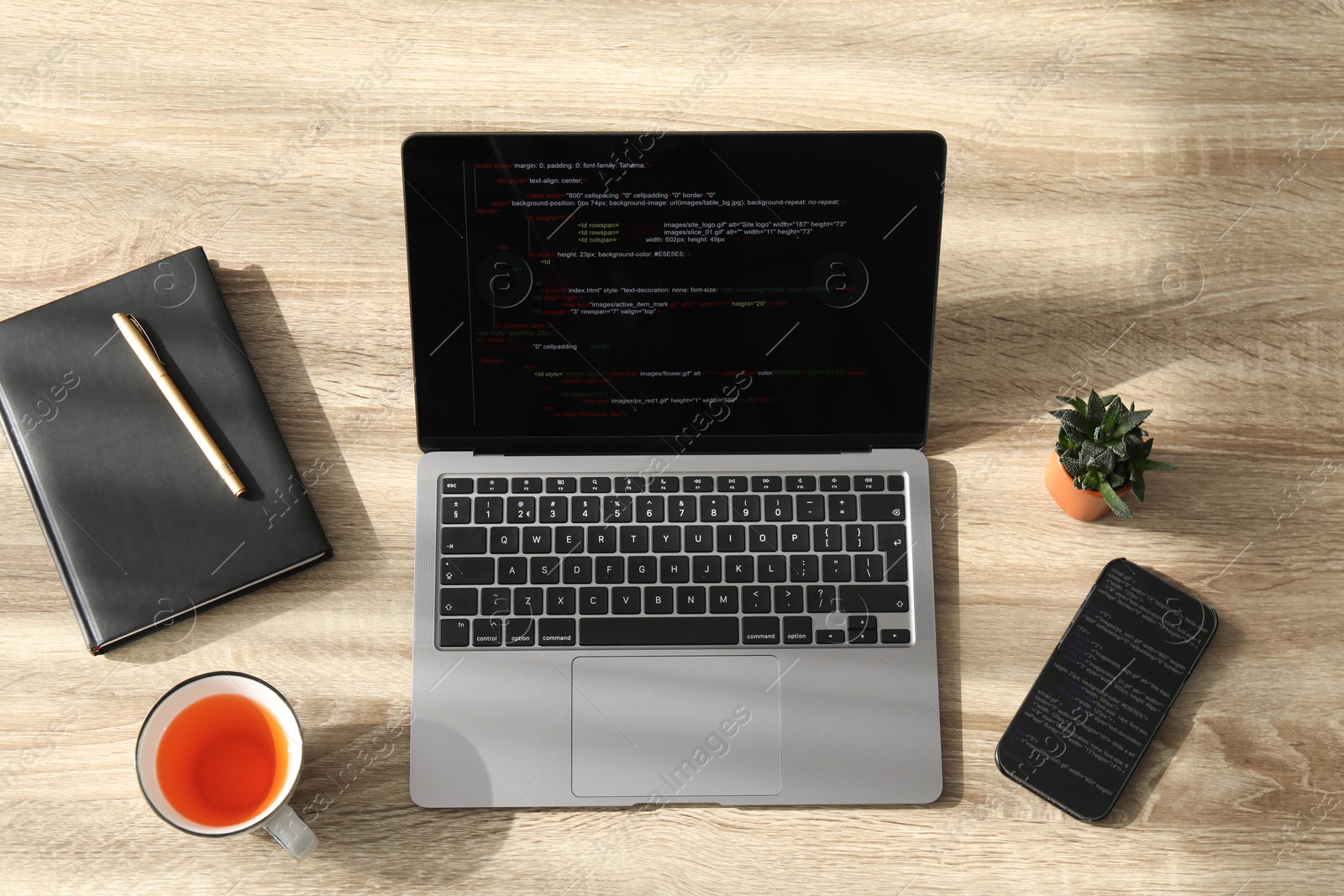 Photo of Programmer's workplace. Modern laptop with unfinished code, smartphone and other supplies on wooden desk, flat lay