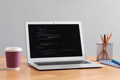 Photo of Programmer's workplace. Modern laptop with unfinished code, paper cup of drink and stationery on desk indoors