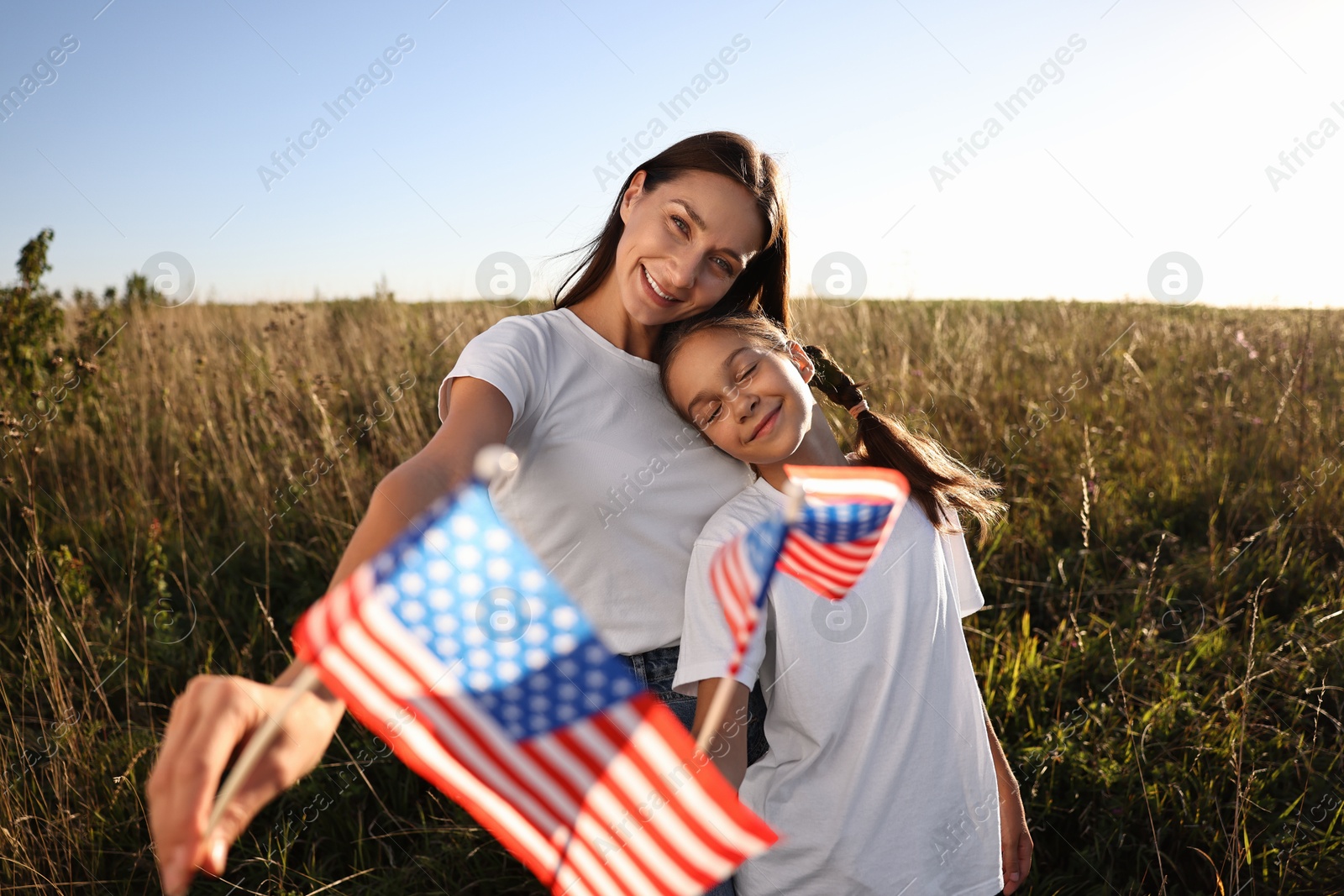 Photo of Happy mother and daughter with flags of USA outdoors, selective focus