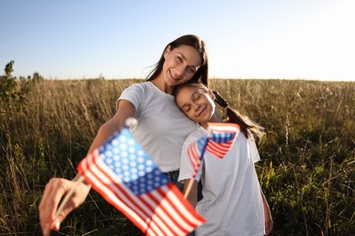 Happy mother and daughter with flags of USA outdoors, selective focus