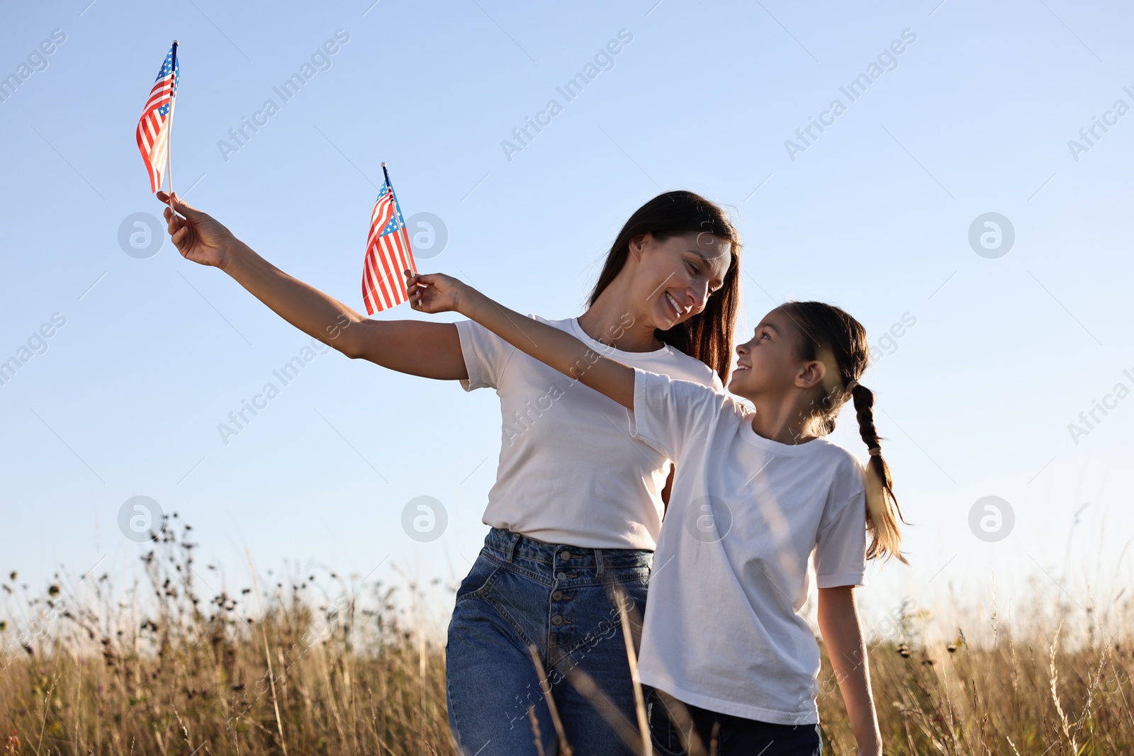 Photo of Happy mother and daughter with flags of USA outdoors, low angle view