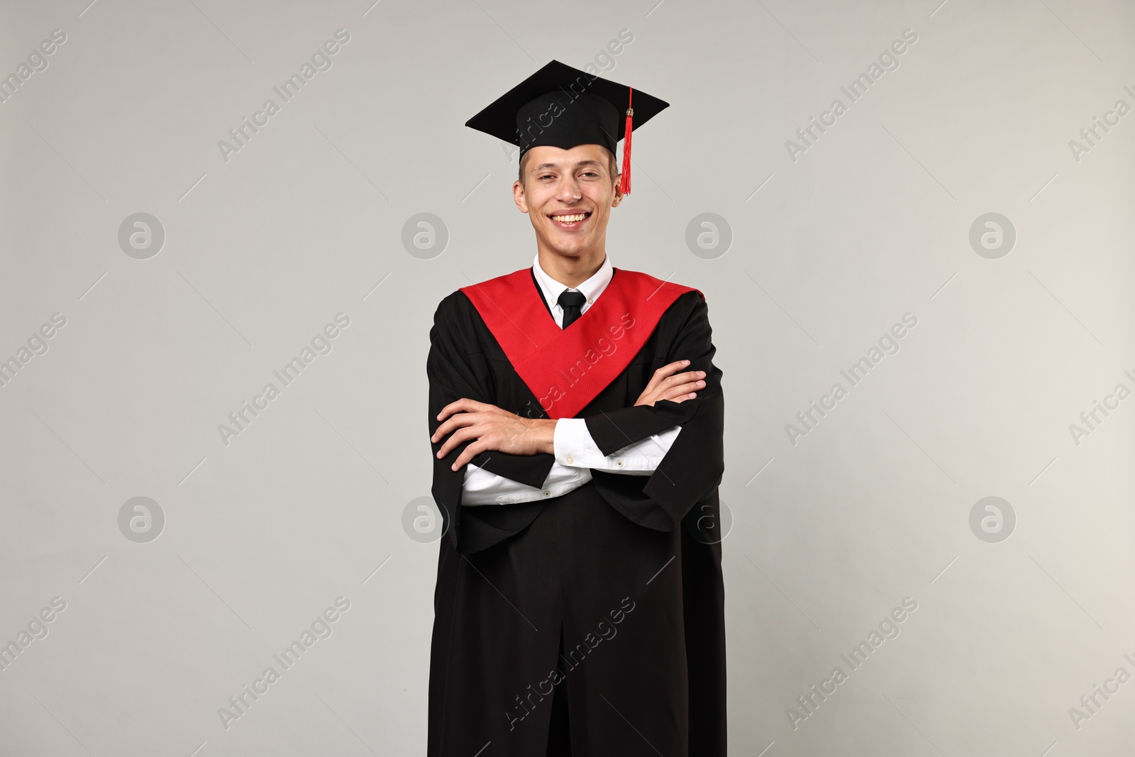 Photo of Happy student with crossed arms after graduation on grey background