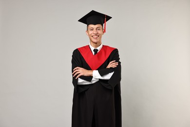 Happy student with crossed arms after graduation on grey background