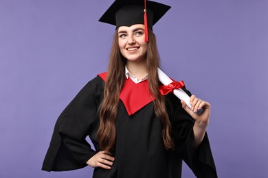 Happy student with diploma after graduation on violet background