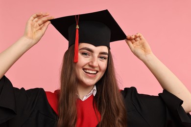 Happy student after graduation on pink background