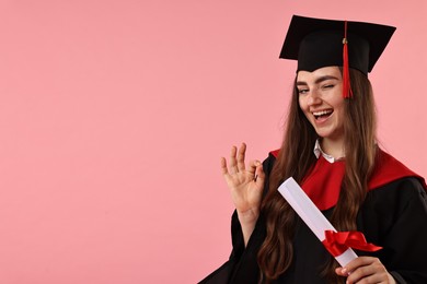 Happy student with diploma after graduation showing ok gesture on pink background. Space for text