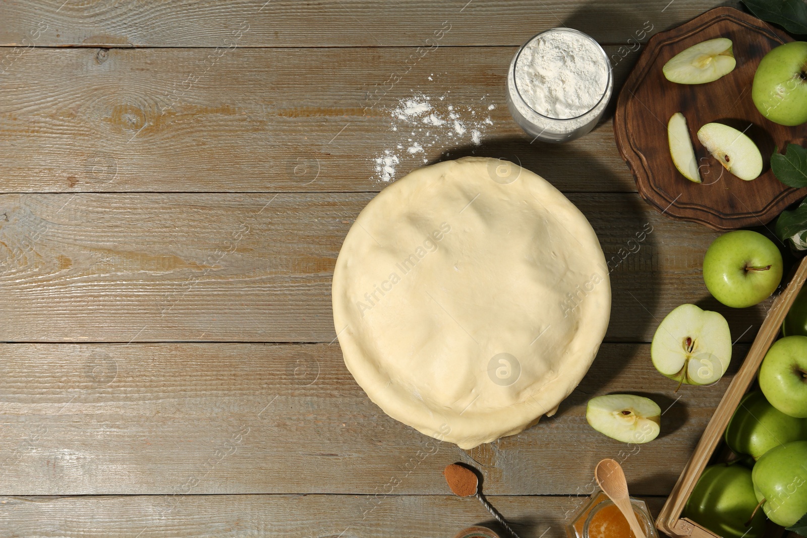 Photo of Raw homemade apple pie and ingredients on wooden table, flat lay. Space for text