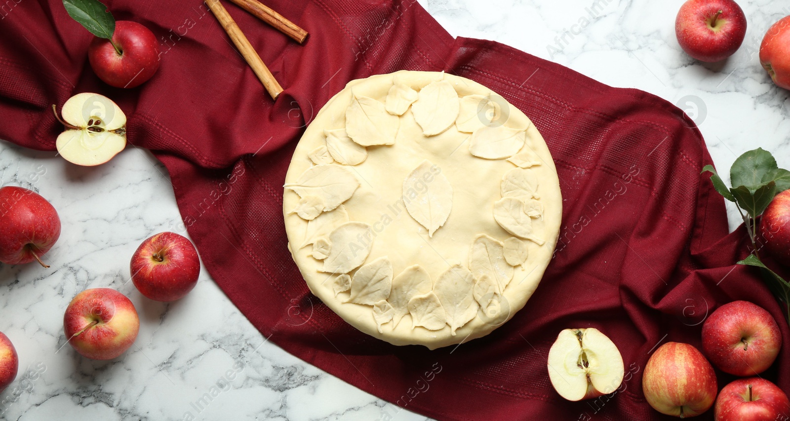 Photo of Raw homemade pie, apples and cinnamon sticks on white marble table, flat lay