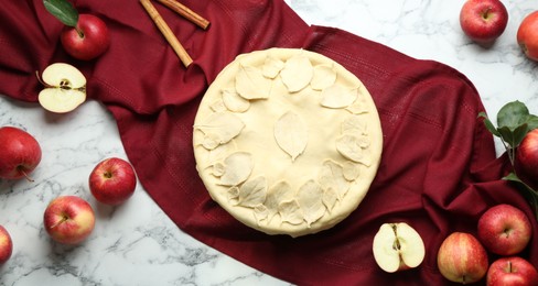 Raw homemade pie, apples and cinnamon sticks on white marble table, flat lay