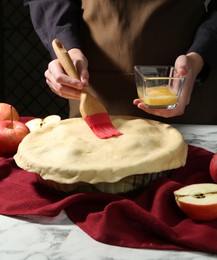 Photo of Woman making homemade apple pie at white marble table, closeup