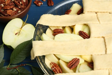 Photo of Raw homemade apple pie with walnuts and ingredients on blue wooden table, closeup