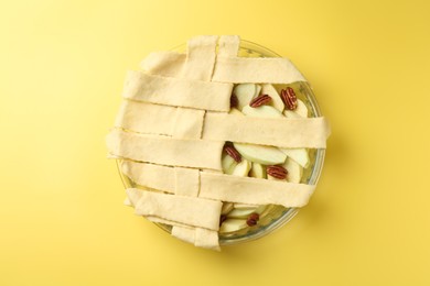 Photo of Raw homemade apple pie with walnuts on yellow background, top view