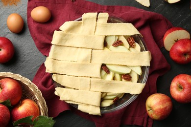 Photo of Flat lay composition with raw homemade apple pie and ingredients on dark textured table